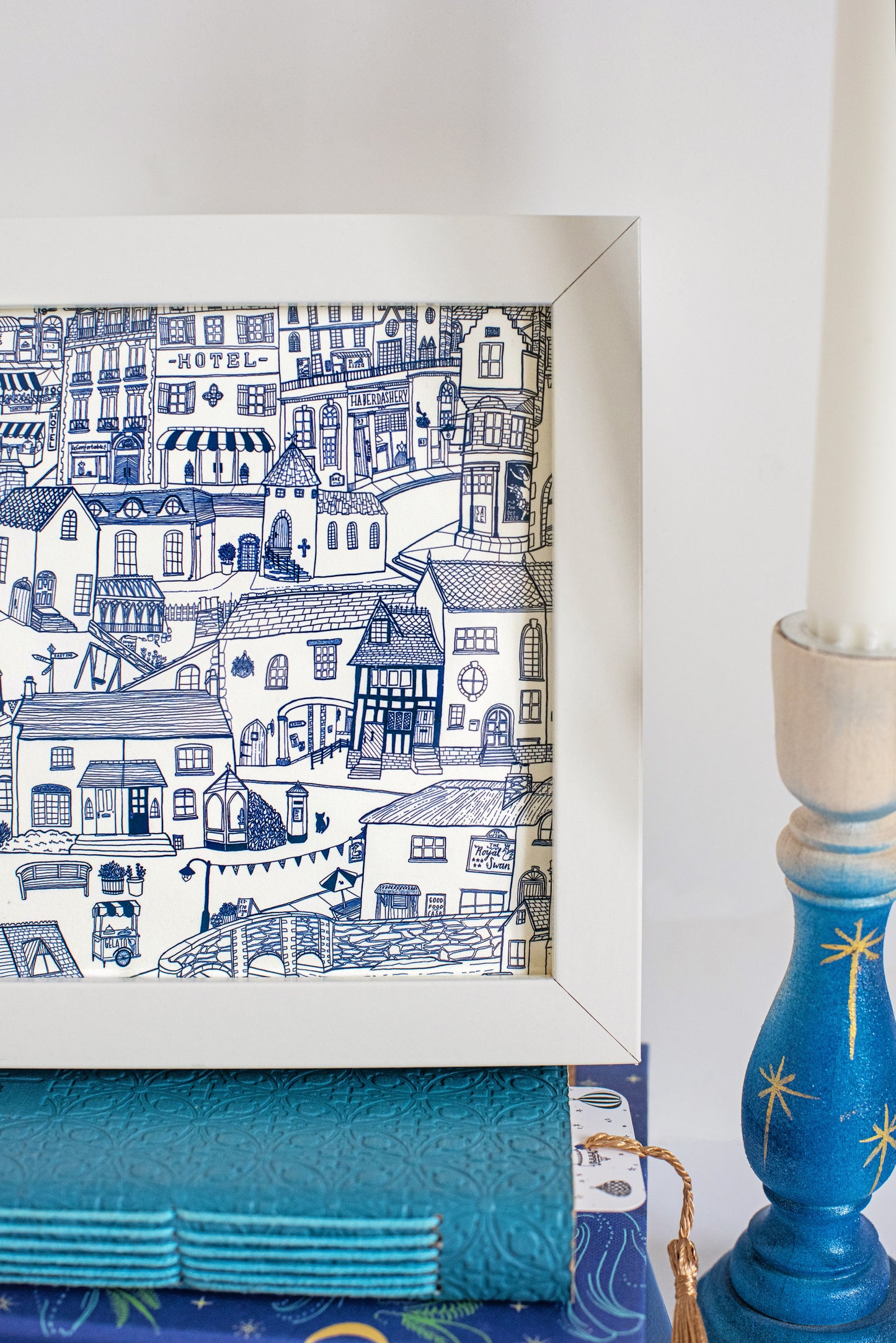 A closeup of the print in its white frame, a blue illustration of a tiny imagined town.