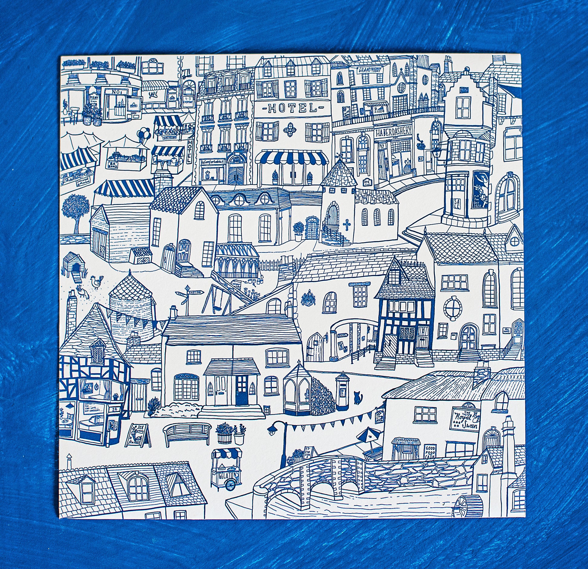 Unframed flatlay of the blue detailed illustration of a charming town scene.